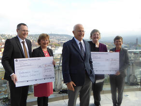Eckhard Hoffmeister steht vor 4 Personen, die 2 Spenden-Checks in Großformat in den Händen halten